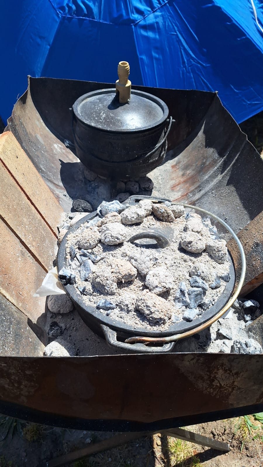 Two Dutch ovens - the top one (with the knob for easy access) has the stew on it and the bottom one is the one the breads were baked in. Note that it stands on top of fire bricks; more coals than this were used when baking breads.